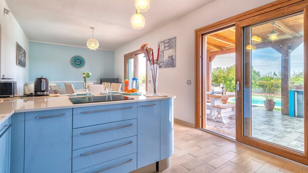 Une cuisine moderne avec un plan de travail bleu, des luminaires suspendus et une vue sur une terrasse extérieure.