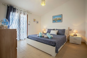 A bedroom with a bed, bedside tables, a nightstand, a wall-mounted picture, and a window with curtains. - Villa Della Felicità with Private Pool, Wi-Fi and Air Conditioning (Sorso)