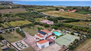Un quartier résidentiel avec une grande maison dotée d’un court de tennis, d’une piscine et offrant une vue sur la mer.