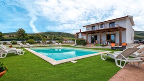 Une piscine avec des chaises longues, une maison dotée d’un balcon et, au loin, un paysage vallonné.
