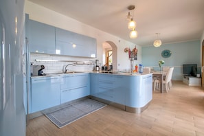 A modern kitchen with blue cabinets, a built-in island, and a dining area with a table and chairs. - Villa Della Felicità with Private Pool, Wi-Fi and Air Conditioning (Sorso)