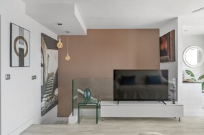A modern living room with a flat-screen TV, glass coffee table, and artwork on the walls.