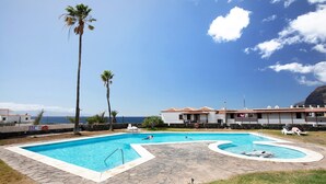 Una piscina con vista despejada al océano, rodeada de palmeras y un edificio con tejado de azulejos.