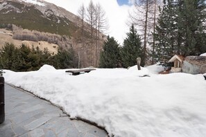 Schneebedeckte Landschaft mit einer Steinsitzbank, einer Holzkonstruktion und einem Berg im Hintergrund.