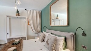 Une chambre à coucher avec un lit, des oreillers, un miroir, une table de chevet et une lampe fixée au mur.