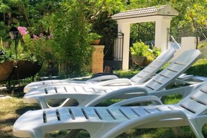 Des fauteuils de jardin en plastique blanc disposés à l’extérieur, un gazebo blanc et des plantes en pot.