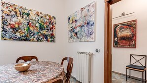 A dining area with a round table, chairs, and a bowl. There are abstract paintings on the walls.