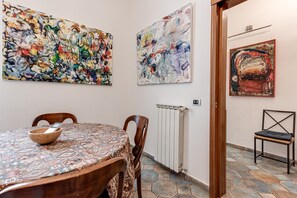 Un coin repas avec une table ronde, des chaises et un saladier. Les murs sont ornés de peintures abstraites.