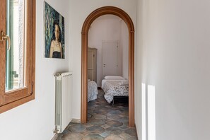 Un couloir avec une porte en bois, un radiateur, un sol carrelé et un lit recouvert d’une couvre-lit à motifs.