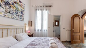 A bedroom with a bed, a painting, a bathroom door, and a tiled floor.