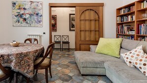 A living room with a round table, chairs, a sofa with cushions, a bookshelf, and a door leading to another room.