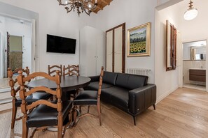 Ein Wohnzimmer mit einem schwarzen Ledersofa, Holzsesseln, einem runden Tisch, einem an der Wand montierten Fernseher und einem Gemälde.