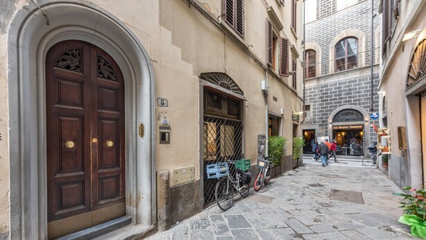 A narrow cobblestone street with a large wooden door, a bicycle, and a building with a sign.