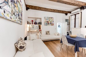 A modern living room with a white sofa, a dining table with chairs, and artwork on the walls.