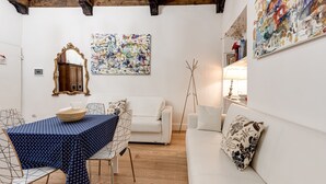A room with a dining table, white sofa, and a large abstract painting.