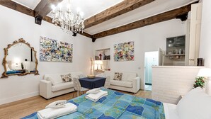 A room with a bed, two white sofas, a chandelier, and artwork on the walls.