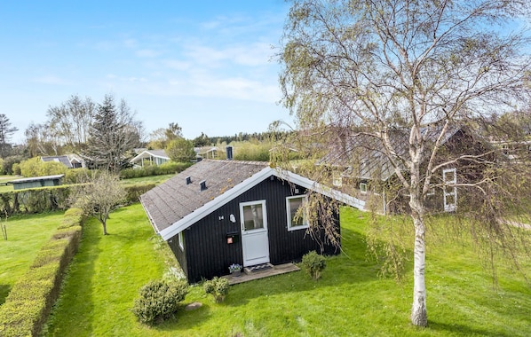 A small black cabin with a sloped roof, surrounded by a well-maintained lawn and a birch tree.