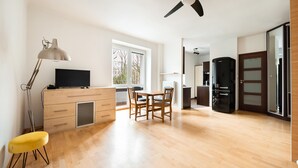 A spacious room with a wooden dining table, chairs, a TV on a wooden cabinet, a ceiling fan, and a window with a view of buildings. - Metro Ratusz Arsenał Comfort Studio (Warszawa)