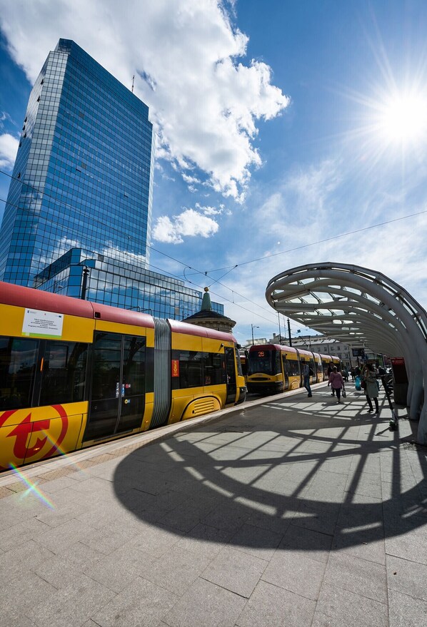 A modern train station with a clear sky, a high-rise building in the background, and a covered waiting area.