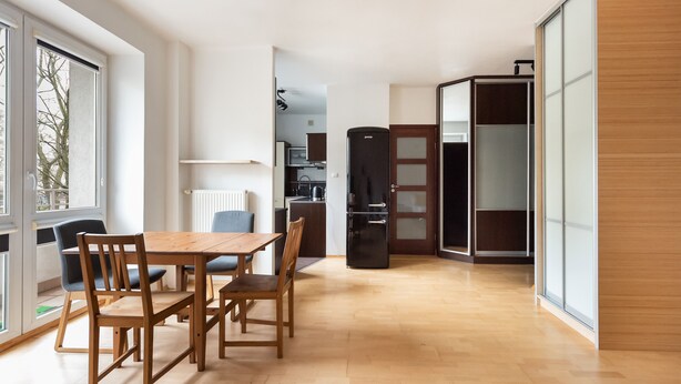A modern kitchen with a black refrigerator, wooden cabinets, and a dining area with a wooden table and chairs. - Metro Ratusz Arsenał Comfort Studio (Warszawa)