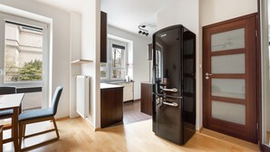 A modern kitchen with a black refrigerator, wooden flooring, and a view of the outside through a window. - Metro Ratusz Arsenał Comfort Studio (Warszawa)