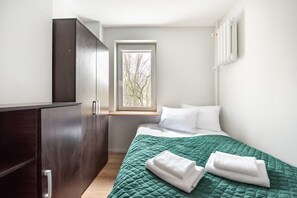 Relax in a serene bedroom with a neatly made bed, dark wardrobe, and a window offering a view of the surrounding trees.