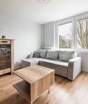 Relax in this serene space with a light grey sofa, wooden coffee table, and a view of the surrounding landscape.