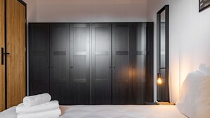 A bedroom with a large dark wooden wardrobe, a neatly made bed, and a wall-mounted light fixture.
