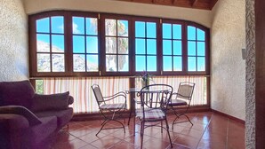 Una habitación iluminada por el sol, con un gran ventanal, una mesa redonda y dos sillas.