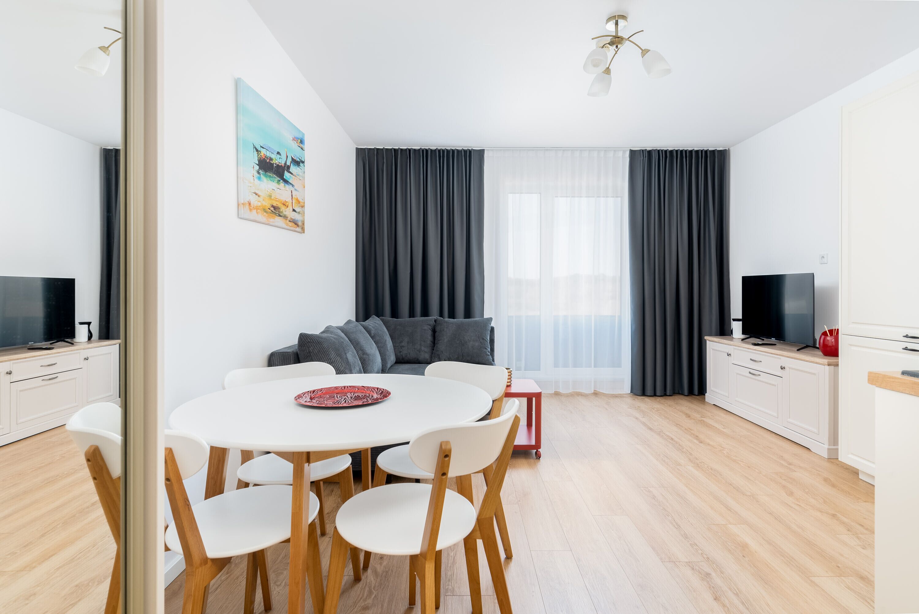 Un salon moderne avec une table à manger blanche, un canapé gris et un téléviseur posé sur un meuble blanc.