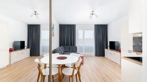 A modern, well-lit room with a dining table, chairs, a sofa, and a TV.