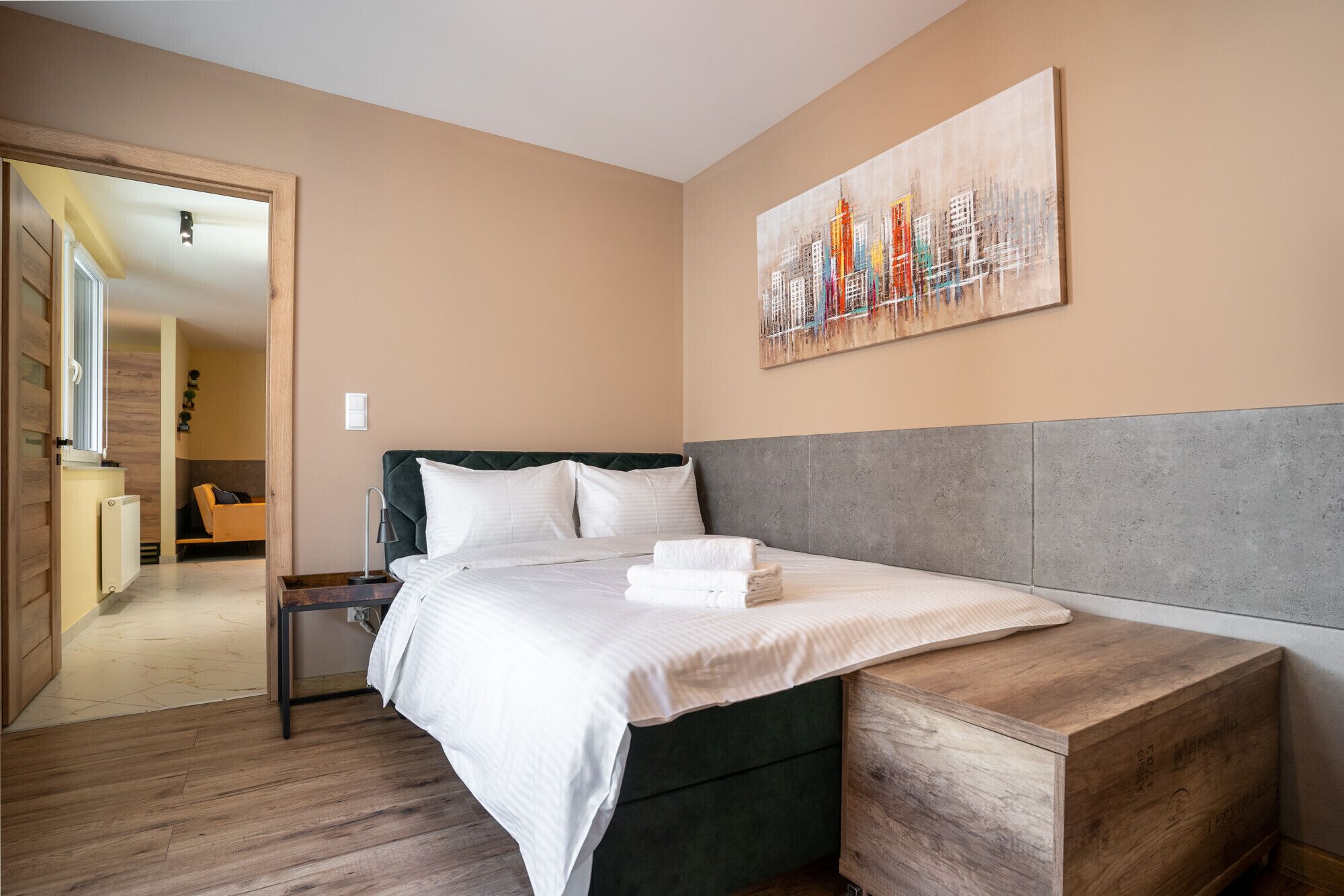 Ein Hotelzimmer mit einem Bett, einer Holzbank, einem Nachttisch und einem Bild an der Wand.