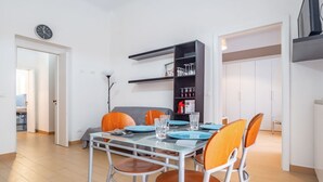 Un comedor con una mesa dispuesta para cuatro personas, sillas, una estantería y un reloj en la pared.