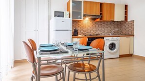 Cocina moderna con horno empotrado, microondas y lavadora. Hay una mesa de comedor con sillas y un salpicadero de azulejos.