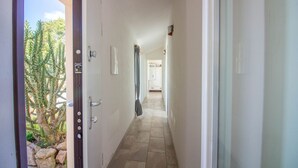 Un pasillo con una puerta que da a una habitación, vista de un cactus afuera y piso de baldosas.