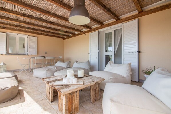 Une vaste terrasse dotée d’une table en bois, de canapés blancs et d’un plafond avec des poutres apparentes.