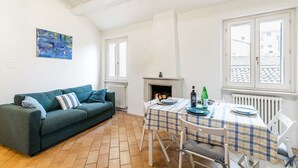 Een woonkamer met een bank, een open haard, een eettafel met stoelen en een raam met uitzicht.