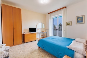 Une chambre à coucher comprenant un lit, un bureau, une télévision, une armoire et un balcon.