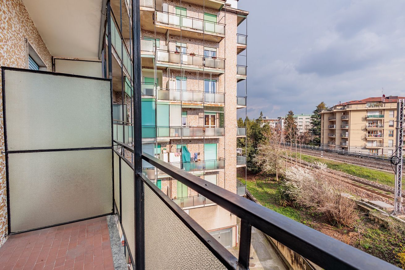 A multi-story building with balconies, a view of a railway track, and a clear sky.