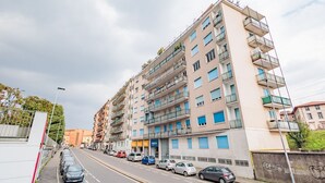 Un edificio residencial de varios pisos con balcones, coches aparcados a lo largo de la calle y un cielo despejado.