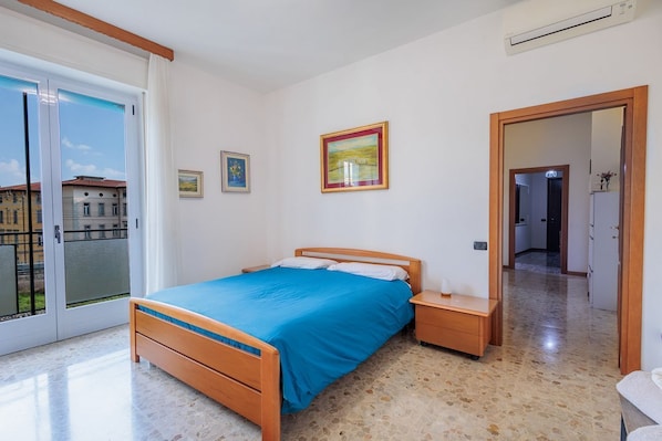 A bedroom with a bed, a nightstand, a door leading to a bathroom, and a window with a view of buildings.