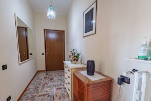 A hallway with a wooden dresser, a mirror, a framed picture, a vase with flowers, and a radiator.