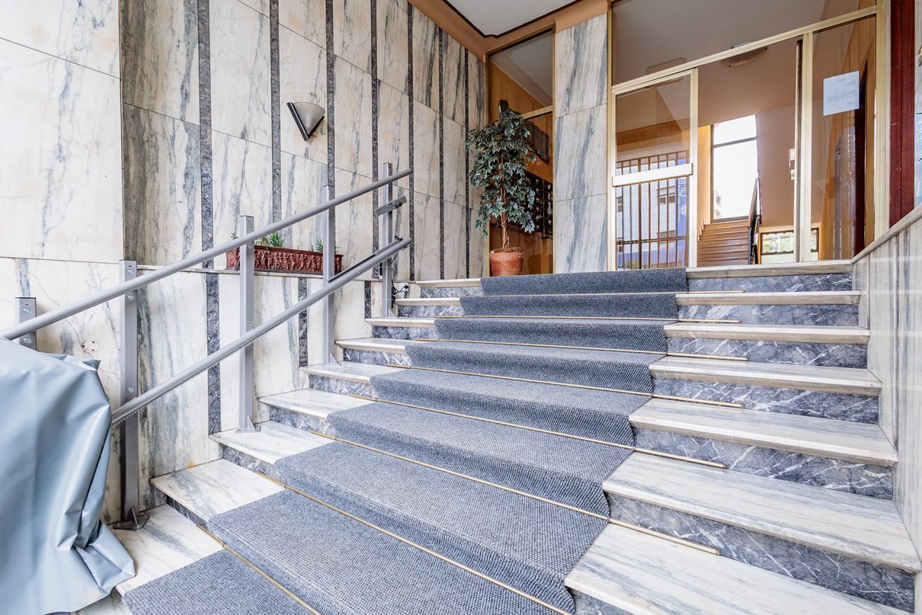 Una escalera de mármol con barandilla de metal, que lleva a una habitación con un gran ventanal.