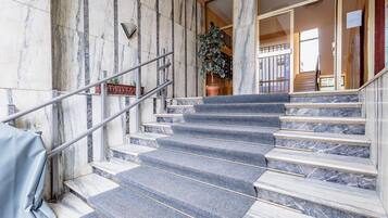 Una escalera de mármol con barandilla de metal, que lleva a una habitación con un gran ventanal.