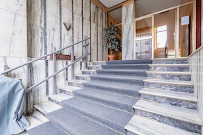 A marble staircase with a metal railing, leading to a room with a large window.