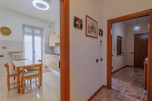 A well-lit hallway with a dining area, kitchen, and a door leading to another room.