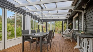 Une terrasse couverte avec une plateforme en bois, une table et des chaises, ainsi que des plantes suspendues.