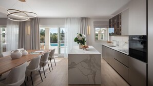 A modern kitchen with a marble island, stainless steel appliances, and a dining area with a wooden table and chairs. - Villa Gabriel Residence (Zminj)