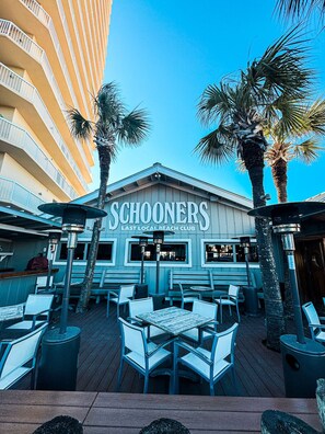 A beach club with outdoor seating and palm trees. - Laketown Wharf 320 |Spacious 3BR with Lakefront Balcony & New Flooring | 5 Pools, 2 Hot Tubs, Gym, Beach Access (Panama City Beach)