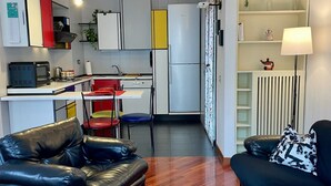 A compact living space with a kitchenette, a black leather sofa, a red dining chair, and a black leather couch. - Bnbook La Residenza di Mondrian (rho)